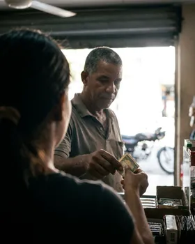 Un cliente entrega un billete doblado sobre el mostrador de un negocio de barrio.