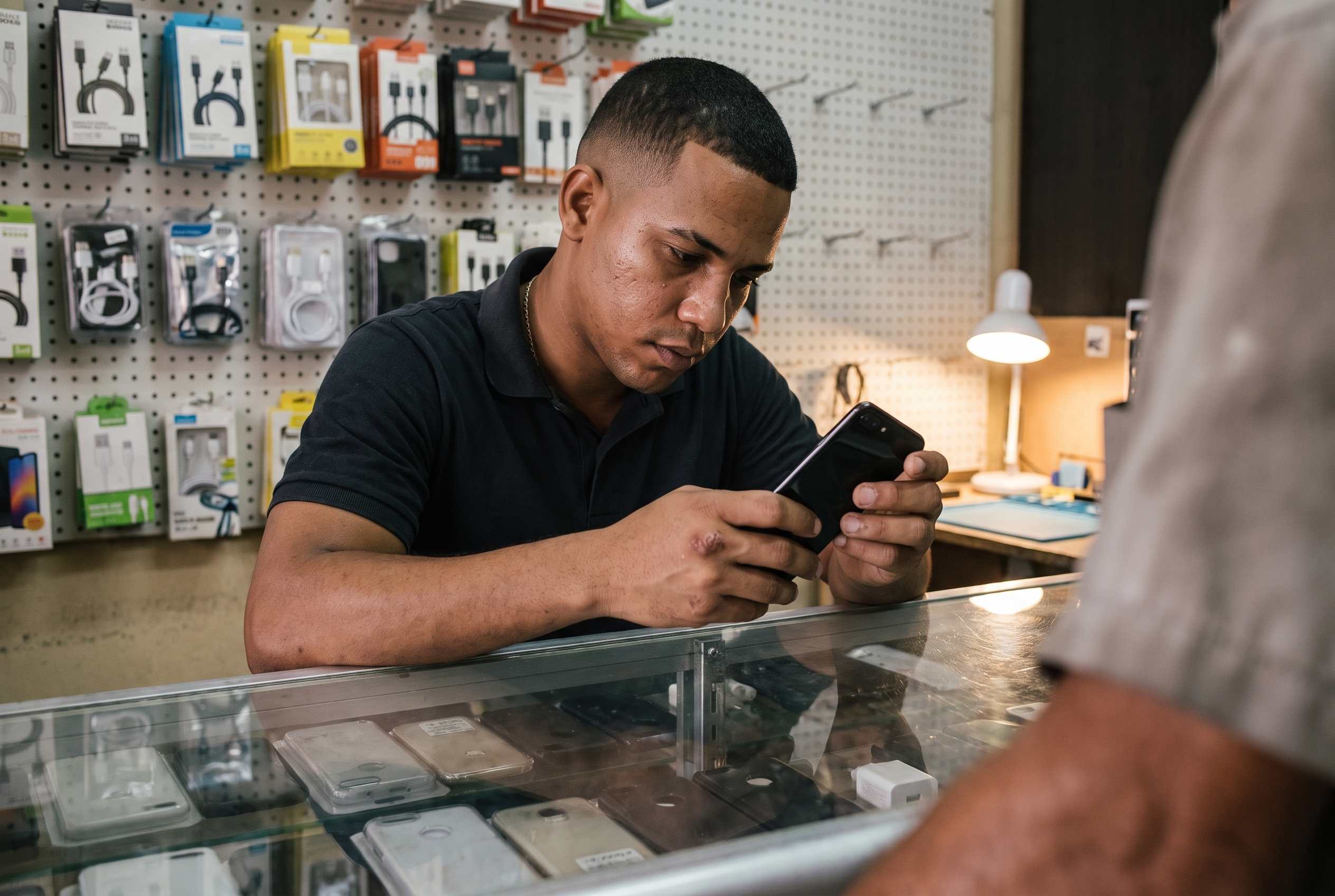 Mostrador de una tienda de celulares con accesorios colgados y un vendedor revisando un equipo.