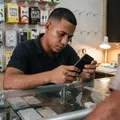 Dependiente de una tienda de celulares examinando un teléfono sobre la vitrina de accesorios.