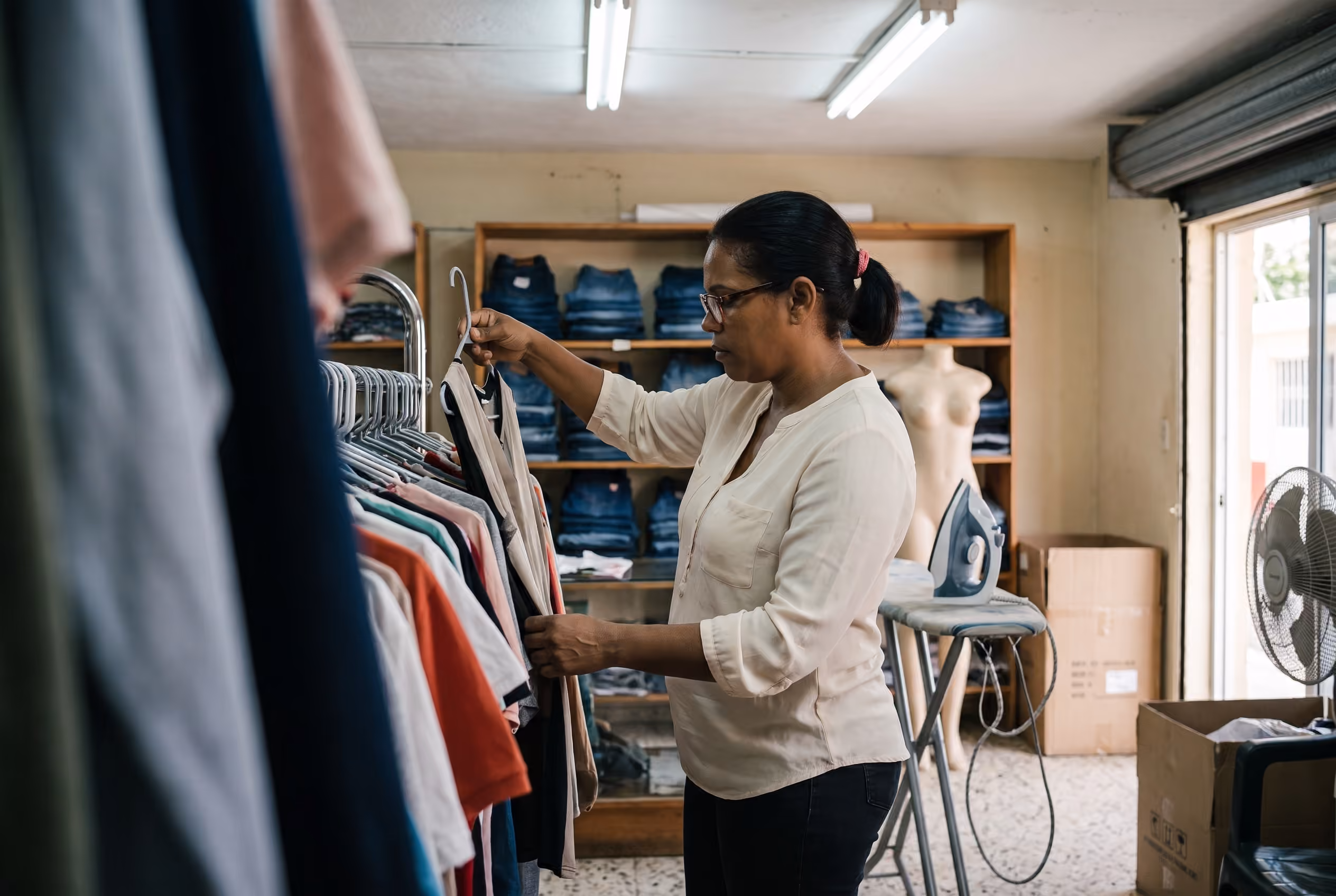 Dueña de una boutique revisando prendas colgadas en un perchero, de espaldas a la entrada.