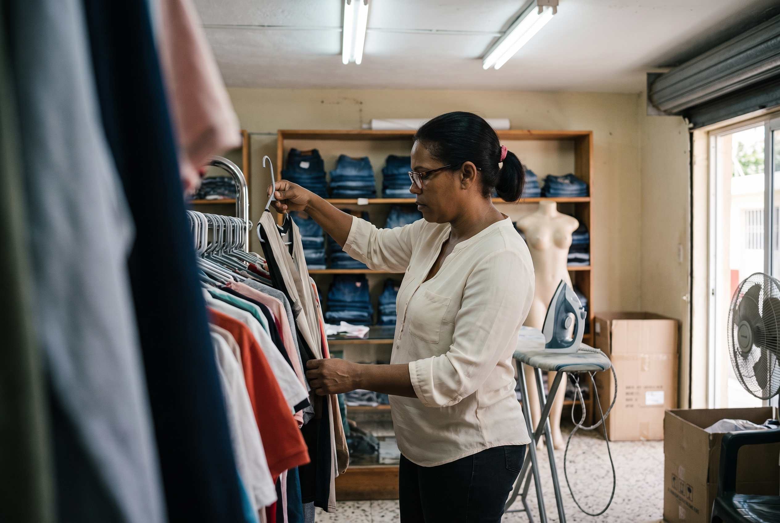 Dueña de una boutique revisando prendas colgadas en un perchero, de espaldas a la entrada.