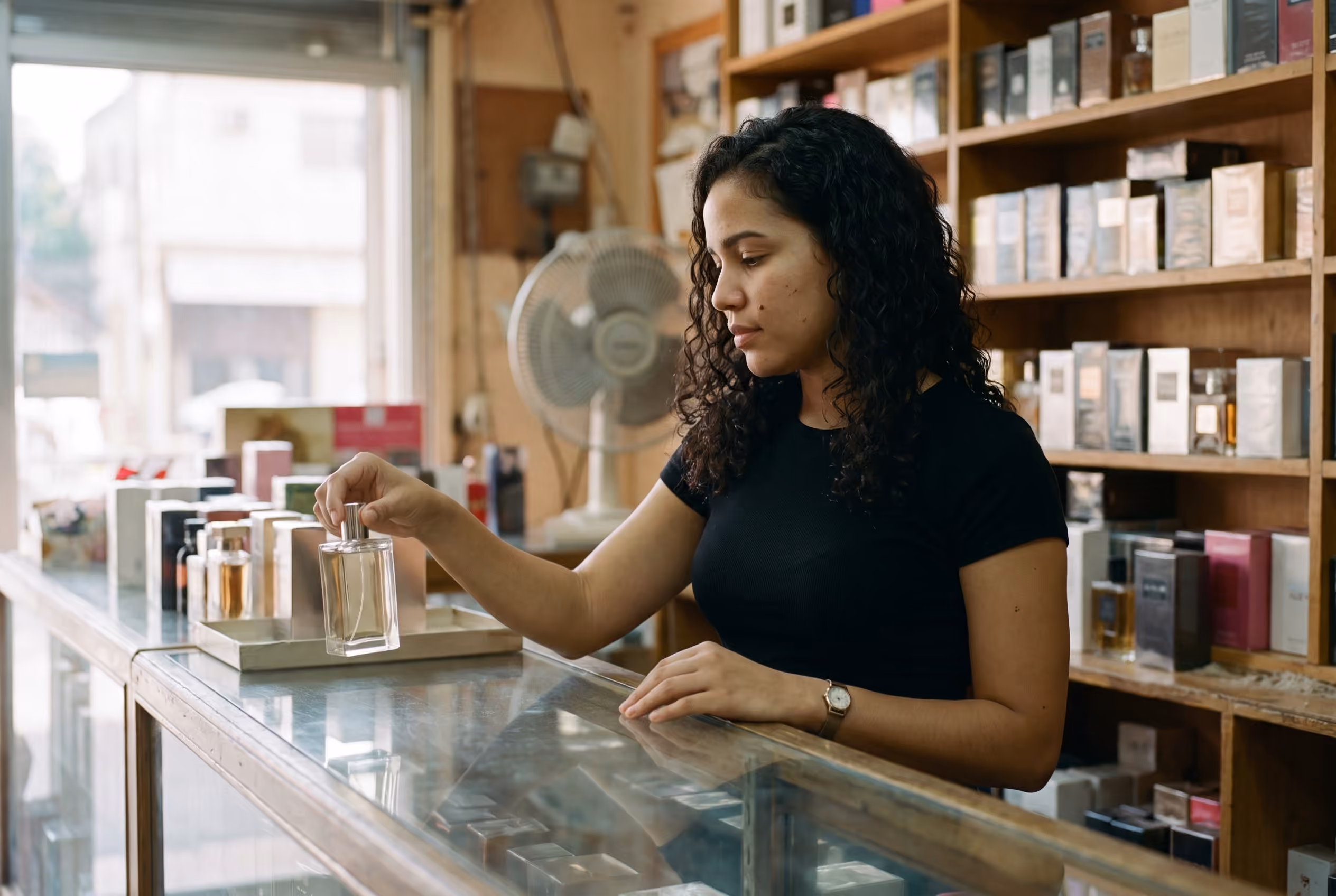 Mostrador de una perfumería con frascos alineados y una vendedora colocando una caja en el estante.