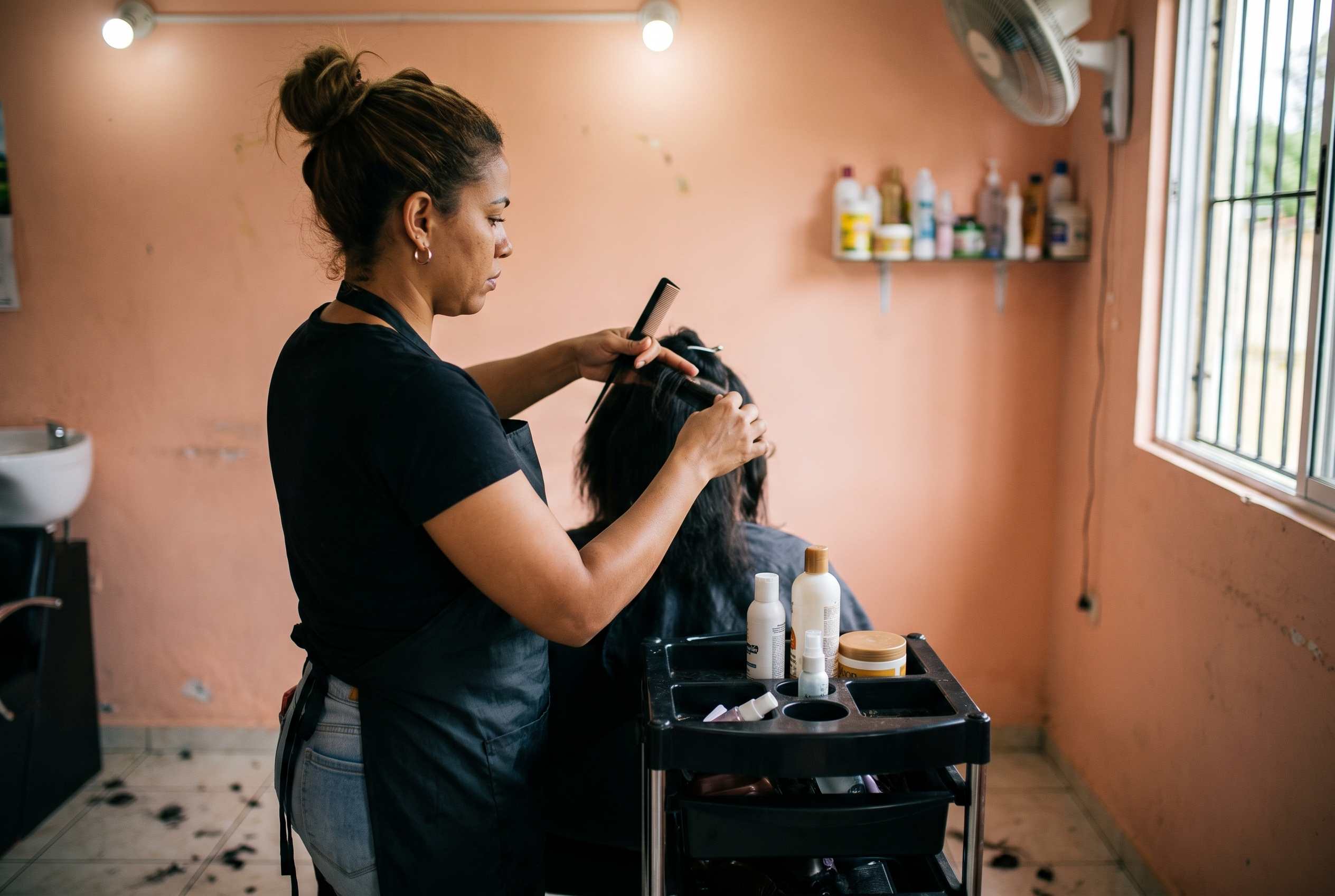 Estilista seccionando el cabello de una clienta en un salón, ambas concentradas en el trabajo.